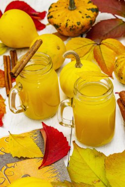 Alkolsüz portakal kokteyli. Bayramlık Cadılar Bayramı içeceği, dekoratif balkabakları, dökülen yapraklar ve tarçın çubukları. Beyaz tahta arka plan, kapat