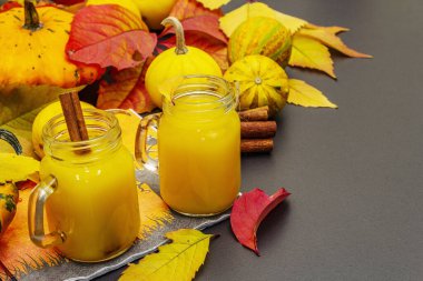 Alkolsüz portakal kokteyli. Bayramlık Cadılar Bayramı içeceği, dekoratif balkabakları, dökülen yapraklar ve tarçın çubukları. Siyah taş arkaplan, boşluğu kopyala