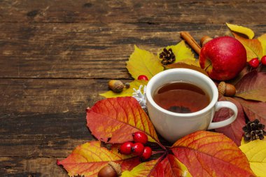 Renkli sonbahar yapraklı sıcak çay, meşe palamudu, tarçın ve gül üzümü. Sonbahar yapraklarıyla iyi bir ruh hali. Eski tahta tahta arka plan, kopyalama alanı