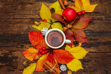 Renkli sonbahar yapraklı sıcak çay, meşe palamudu, tarçın ve gül üzümü. Sonbahar yapraklarıyla iyi bir ruh hali. Eski tahta arka plan, üst görünüm