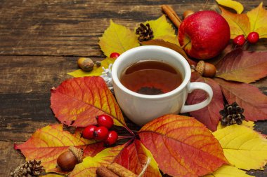 Renkli sonbahar yapraklı sıcak çay, meşe palamudu, tarçın ve gül üzümü. Sonbahar yapraklarıyla iyi bir ruh hali. Eski tahta arka plan, kapat