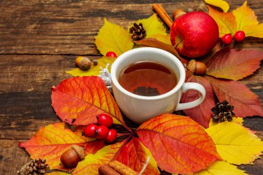Renkli sonbahar yapraklı sıcak çay, meşe palamudu, tarçın ve gül üzümü. Sonbahar yapraklarıyla iyi bir ruh hali. Eski tahta arka plan, kapat