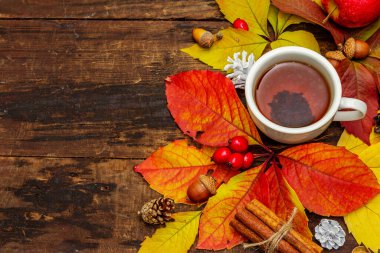 Renkli sonbahar yapraklı sıcak çay, meşe palamudu, tarçın ve gül üzümü. Sonbahar yapraklarıyla iyi bir ruh hali. Eski tahta arka plan, üst görünüm