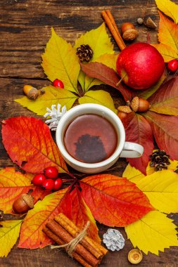 Renkli sonbahar yapraklı sıcak çay, meşe palamudu, tarçın ve gül üzümü. Sonbahar yapraklarıyla iyi bir ruh hali. Eski tahta arka plan, üst görünüm