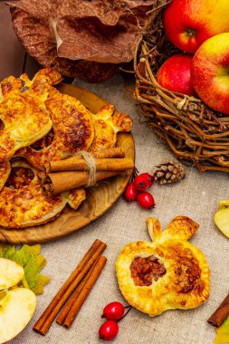 Ev yapımı lezzetli elmalı tatlı. Taze fırın, porsiyonlu puf böreği. Kokulu tarçın çubukları, olgun elmalar, sonbahar yaprakları, deniz tuzu. Tahta masa, kapat.