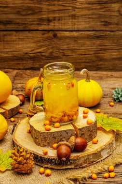 Küçük cam kavanozlarda taze böğürtlenli ve sonbahar dekorlu vitaminli deniz dikenli çay. Sonbahar yaprakları, balkabakları ve meşe palamudu. Eski tahta kaplama arka plan, kapat