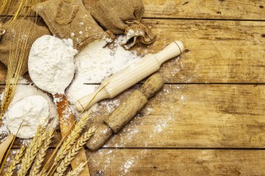 Torbalarda un, tahıl kulakları, kaşıklar ve tahta raptiyeler. Pişirme konsepti, tahta tahta arka plan, üst görünüm