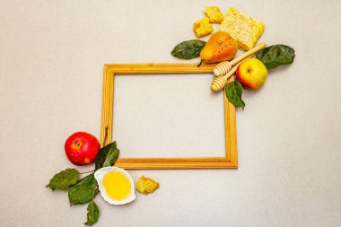Geleneksel Rosh Hashanah sembollü ahşap çerçeve. Yeni yıl Yahudi bayramında taze elmalar, armutlar, sıvı bal ve bal petekleri. Hafif taş arkaplan, üst görünüm