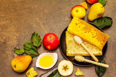 Rosh Hashanah geleneksel sembollerle kutlama konsepti. Yeni yıl Yahudi bayramında taze elmalar, armutlar, sıvı bal ve bal petekleri. Kahverengi taş arkaplan, üst görünüm