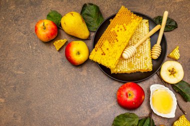 Rosh Hashanah geleneksel sembollerle kutlama konsepti. Yeni yıl Yahudi bayramında taze elmalar, armutlar, sıvı bal ve bal petekleri. Kahverengi taş arkaplan, üst görünüm