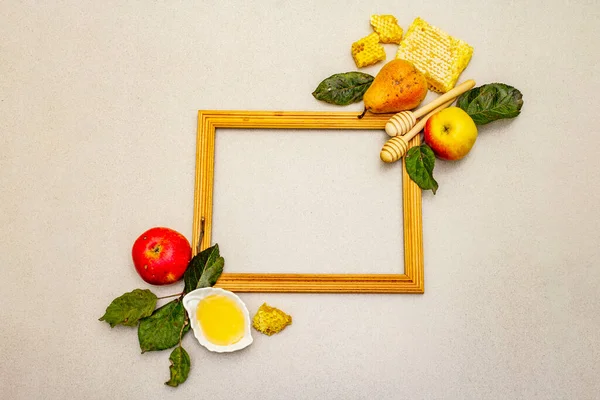 Wooden frame with Rosh Hashanah traditional symbols. Jewish New Year holiday with fresh apples and pears, liquid honey and honeycombs. Light stone concrete background, top view