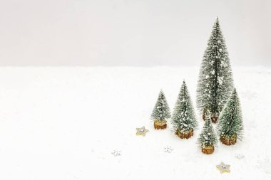 Yeni yıl dekoru olan küçük dekoratif Noel ağaçları. Kar taneleri, parlayan yıldızlar ve beyaz macun arka planda yapay kar, boşluğu kopyala