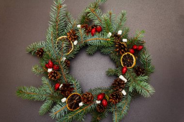 Sıfır atık Noel çelengi köknar ağacı dalları, gül ağacı meyveleri, kuru limon dilimleri ve marşmelovlarla. Yeni yıl iyi ruh hali, taş beton arka plan, üst manzara