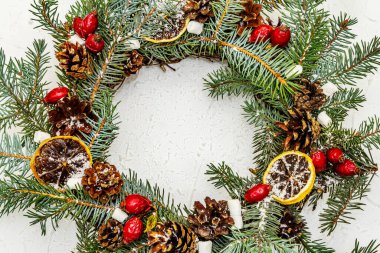 Sıfır atık Noel çelengi köknar ağacı dalları, gül ağacı meyveleri, kuru limon dilimleri ve marşmelovlarla. Yeni yıl iyi ruh hali, taş beton arka plan, üst manzara
