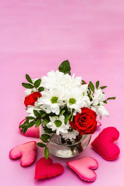Cam vazoda bir buket taze çiçek ve yumuşak kalpler. Sevgililer günü ya da düğün konsepti. Yumuşak pembe desenli arka plan