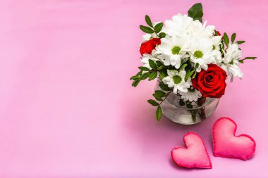 Cam vazoda bir buket taze çiçek ve yumuşak kalpler. Sevgililer günü ya da düğün konsepti. Yumuşak pembe desenli arka plan