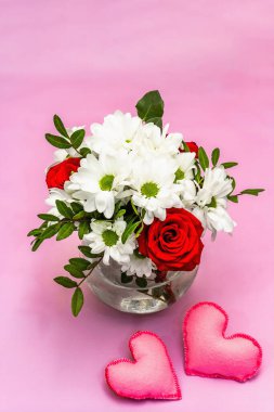 Cam vazoda bir buket taze çiçek ve yumuşak kalpler. Sevgililer günü ya da düğün konsepti. Yumuşak pembe desenli arka plan