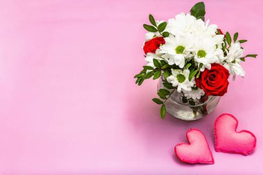 Cam vazoda bir buket taze çiçek ve yumuşak kalpler. Sevgililer günü ya da düğün konsepti. Yumuşak pembe desenli arka plan