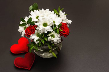 Cam vazoda bir buket taze çiçek ve yumuşak kalpler. Sevgililer günü ya da düğün konsepti. Siyah taş beton arka plan