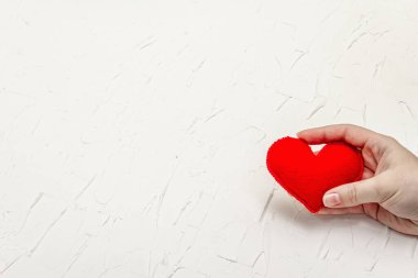 Sevgililer Günü konsepti. Kadın eli ev yapımı kırmızı bir keçeli kalp tutuyor. Beyaz macun desenli arkaplan