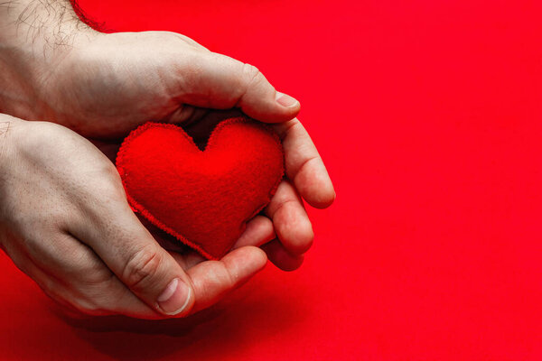 Valentine's Day concept. Male hands are holding a homemade felt heart. Bright red textured background