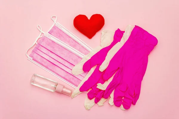 Red heart with medical protection masks and gloves on light pink background, copy space. Concept of healthcare, self-defense