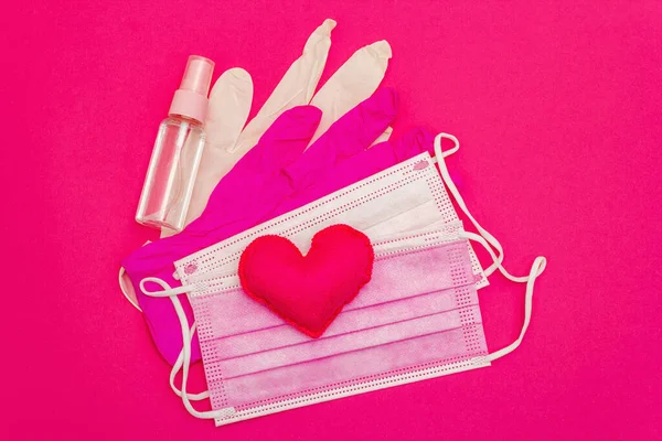 Red heart with medical protection masks and gloves on bright pink background, copy space. Concept of healthcare, self-defense