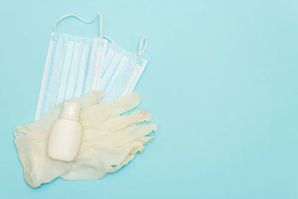 Surgical protection masks, sanitizer and gloves isolated on light blue background. Medical products for personal hygiene and the prevention of viral diseases. Coronavirus, COVID-19 pandemic, 2019-nCoV worldwide concept