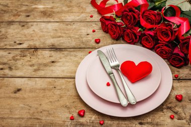 Romantik yemek masası. Sevgililer günü ya da anneler günü için aşk konsepti, düğün çatal bıçak takımı. Bir buket taze burgundy gül, eski ahşap tahta arka plan