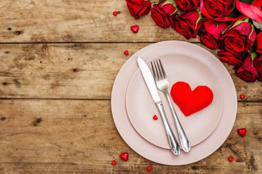 Romantik yemek masası. Sevgililer günü ya da anneler günü için aşk konsepti, düğün çatal bıçak takımı. Bir buket taze burgundy gül, eski ahşap tahta arka plan