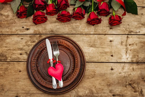 Romantic dinner table. Love concept for Valentine\'s or mother\'s day, wedding cutlery. Bouquet of fresh burgundy roses, vintage wooden boards background, rustic style