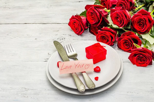 Romantic dinner table. Love concept for Valentine\'s or mother\'s day, wedding cutlery. Bouquet of fresh burgundy roses, white vintage wooden boards background
