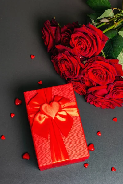 Bouquet of fresh burgundy roses and gift box on a black stone concrete background. Fragrant red flowers, gift concept for Valentine's Day, Wedding or Birthday