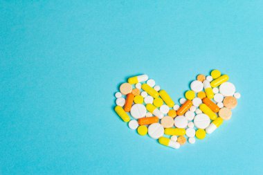 Kalp hastalıklarının tedavisi için çeşitli ilaç hapları, haplar ve kapsüller. Kalp şeklinde, eğimli mavi arkaplan. Metin için alanı kopyala