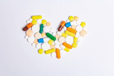Beyaz arka planda izole edilmiş kalp hastalıklarının tedavisi için çeşitli ilaç hapları, haplar ve kapsüller. Kalp şekli, metin için boşluk kopyala