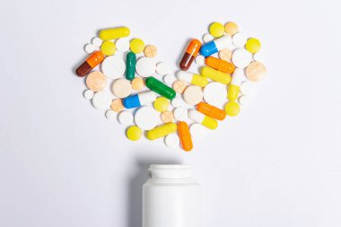 Beyaz arka planda izole edilmiş kalp hastalıklarının tedavisi için çeşitli ilaç hapları, haplar ve kapsüller. Kalp şekli ve ilaç şişesi, metin için kopyalama alanı