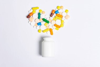 Beyaz arka planda izole edilmiş kalp hastalıklarının tedavisi için çeşitli ilaç hapları, haplar ve kapsüller. Kalp şekli ve ilaç şişesi, metin için kopyalama alanı