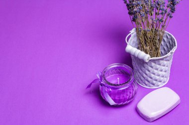 Tek renkli lavanta spa konsepti. Kovadaki güzel kokulu çiçekler, doğal sabun ve mor bir mum. Matte leylak arkaplan, metin için yer