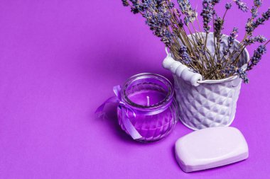 Tek renkli lavanta spa konsepti. Kovadaki güzel kokulu çiçekler, doğal sabun ve mor bir mum. Matte leylak arkaplan, metin için yer