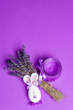 Tek renkli lavantalı Paskalya konsepti. Kokulu çiçekler, doğal mor mum ve sevimli tavşan. Matte leylak arkaplan, metin için yer
