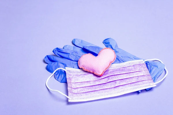 Lilac heart with medical protection masks and gloves on light purple background, copy space. Concept of healthcare, self-defense