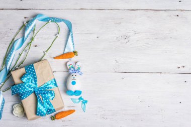 El yapımı geleneksel Paskalya sembolleri. Yumurtadan tatlı bir tavşan, hediye kutusu, mavi tonlarda şenlik dekoru. Beyaz ahşap arkaplan, üst görünüm