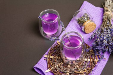 Taze lavanta menekşeli kokteyl, siyah taş beton arka planda. İçki bardakları, kuru buket, hasır tezgah, leylak peçete, fotokopi alanı.