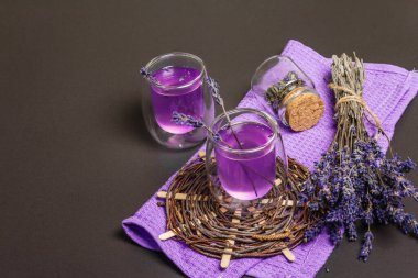 Taze lavanta menekşeli kokteyl, siyah taş beton arka planda. İçki bardakları, kuru buket, hasır tezgah, leylak peçete, fotokopi alanı.