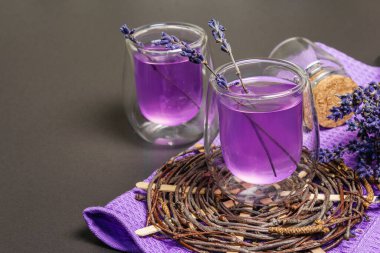 Taze lavanta menekşeli kokteyl, siyah taş beton arka planda. İçki bardakları, kuru buket, hasır tezgah, leylak peçete, kapatın.