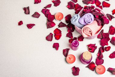 Kurumuş gül yaprakları, kokulu mumlar ve yumuşak havluyla çiçek ve spa konsepti. Doğal gül yağı, hafif taş arkaplan, üst manzara.