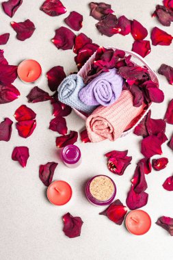 Kurumuş gül yaprakları, kokulu mumlar ve yumuşak havluyla çiçek ve spa konsepti. Doğal gül yağı, hafif taş arkaplan, üst manzara.
