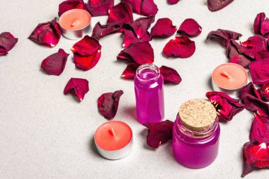Kurumuş gül yaprakları, kokulu mumlar ve yumuşak havluyla çiçek ve spa konsepti. Doğal gül yağı, hafif taş arkaplan, yakın plan.