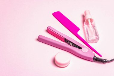 Minimalist saç bakım konsepti. Saç düzleştirici, fırça, sprey ve yağ. Hassas pastel pembe arka plan