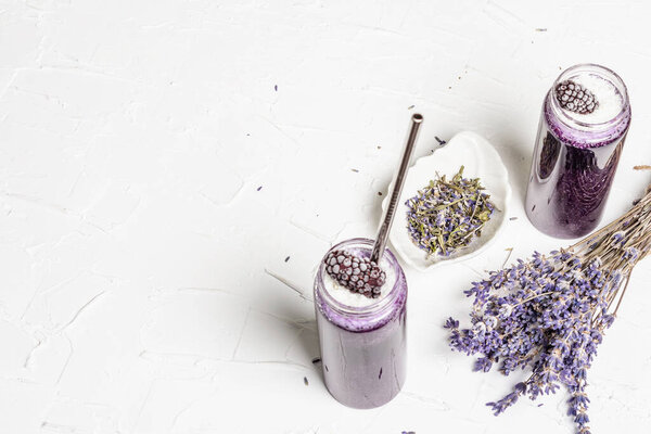 Лавандовый смузи с кокосовыми хлопьями и замороженной ежевикой. Букет сухих цветов, лиловая салфетка. Белый шпаклевочный фон, вид сверху